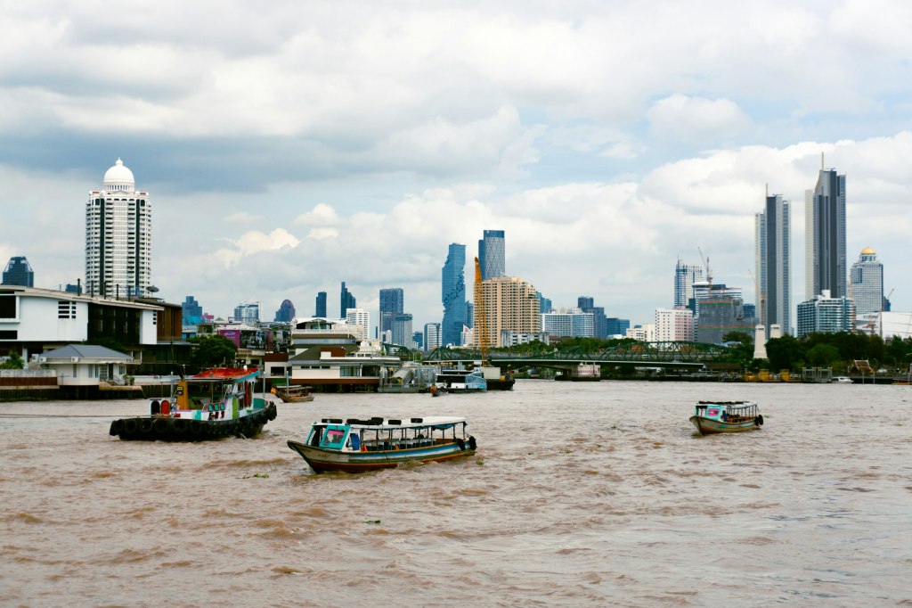 Boats on the wide Chao Phraya river with the Bangkok skyline behind