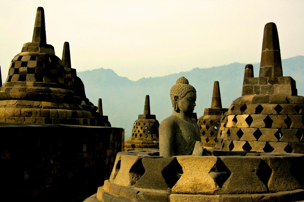 Stone Buddha statue among bell-shaped stupas at Borobudur in Central Java, Indonesia