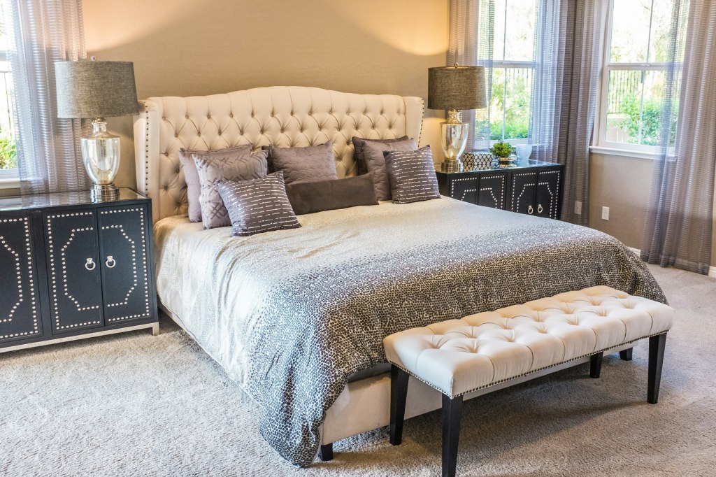 A bedroom with a tufted headboard and soft grey bedding