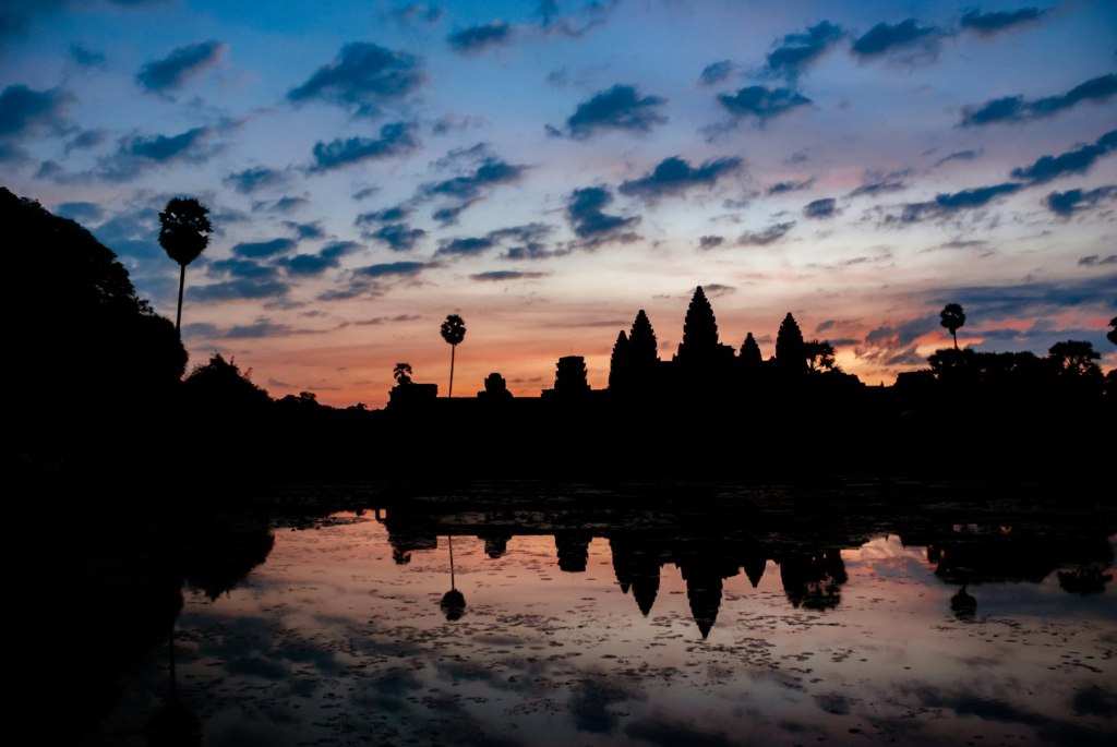 Silhouette of an Angkor temple under a cloudy sky at golden hour