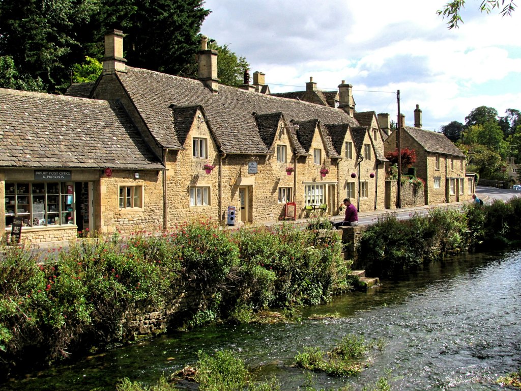 Honey-colored stone cottages beside a river in a Cotswolds village