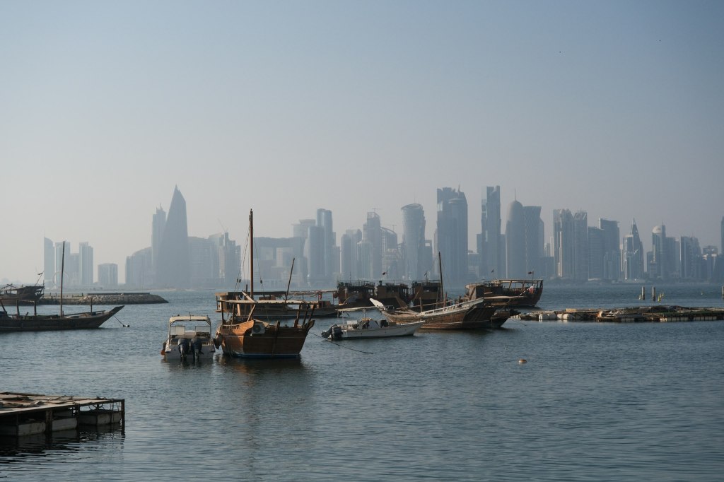 Traditional wooden dhow boats in a Doha harbor with the city skyline behind