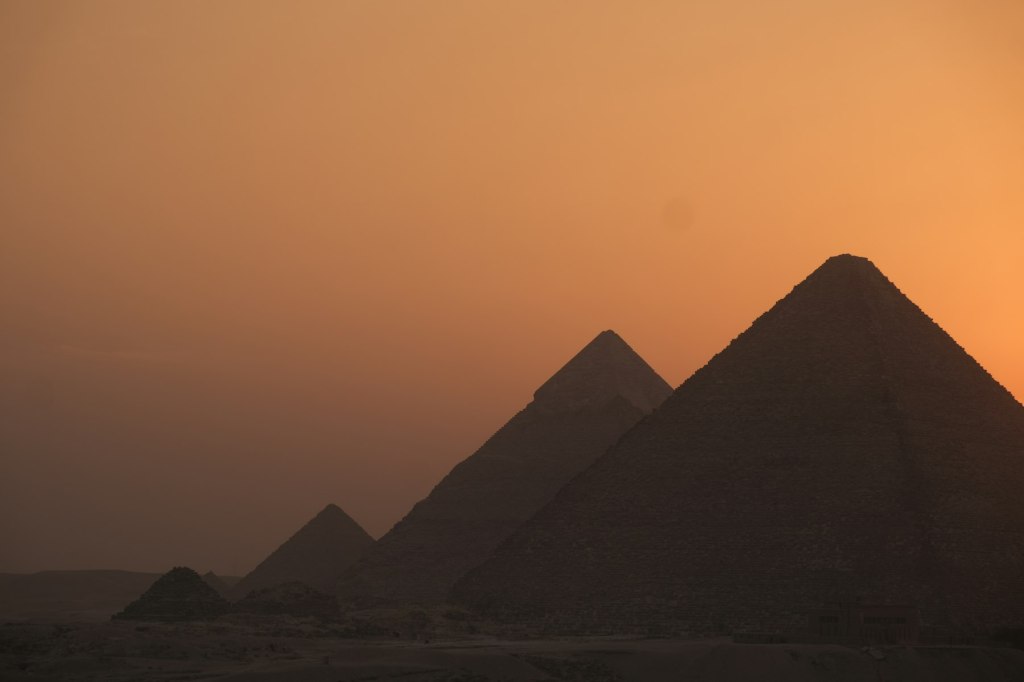 Sun setting behind the pyramids of Giza across the desert