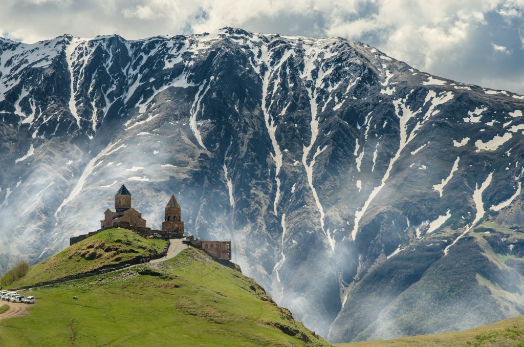 Gergeti Trinity Church on a green ridge beneath snowy Mount Kazbek in Kazbegi, Georgia