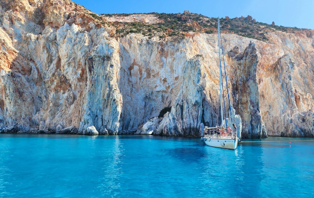A boat on calm blue Mediterranean water beside a mountainous coast