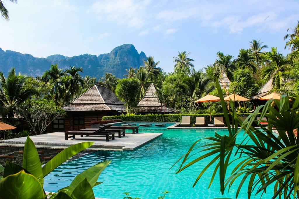 Quiet resort swimming pool with a wooden bench in a tropical garden, evoking a Chiang Mai luxury stay