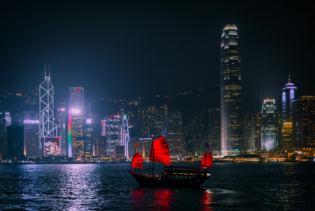 A traditional junk boat with red sails on Victoria Harbour at night, near West Kowloon in Hong Kong